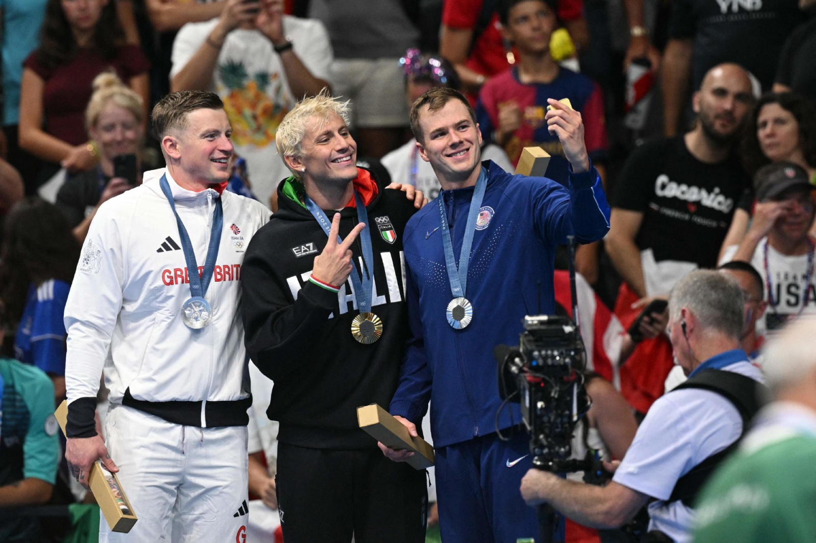 (L-R) Silver medallists Britain's Adam Peaty, gold medallist Italy's Nicolo Martinenghi and US' Nic Fink stand on the podium after the men's 100m breaststroke swimming event during the Paris 2024 Olympic Games at the Paris La Defense Arena in Nanterre, we