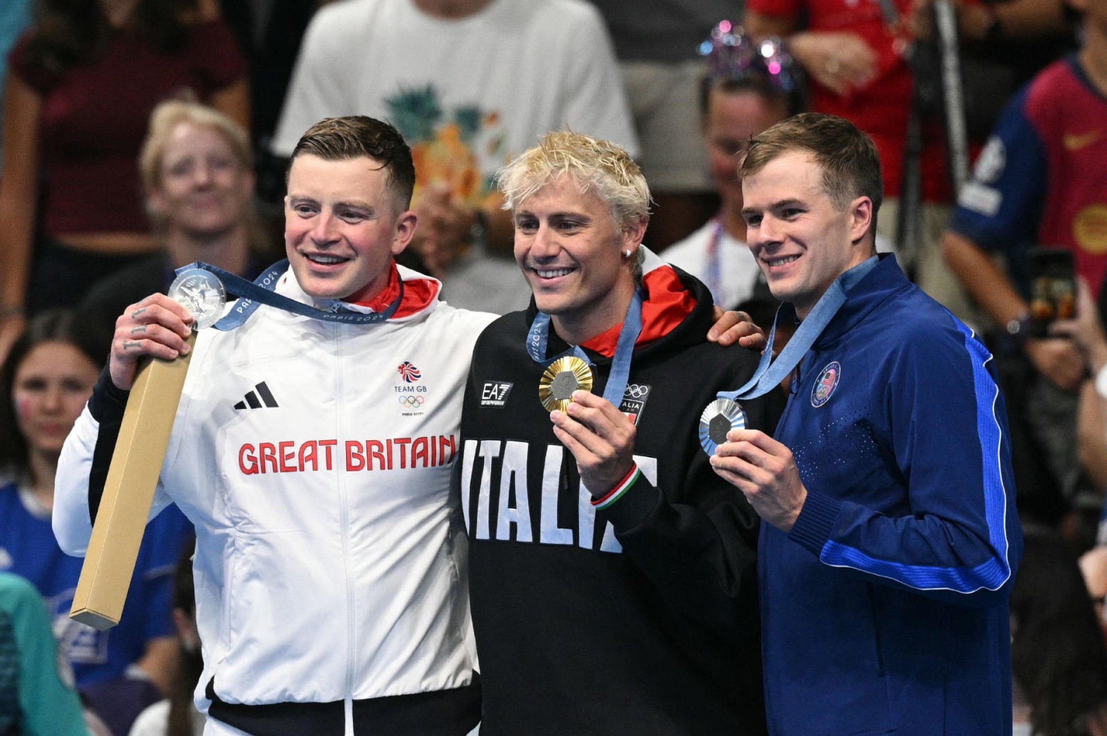 (L-R) Silver medallist Britain's Adam Peaty, gold medallist Italy's Nicolo Martinenghi and silver medallist US' Nic Fink stand on the podium after the men's 100m breaststroke swimming event during the Paris 2024 Olympic Games at the Paris La Defense Arena